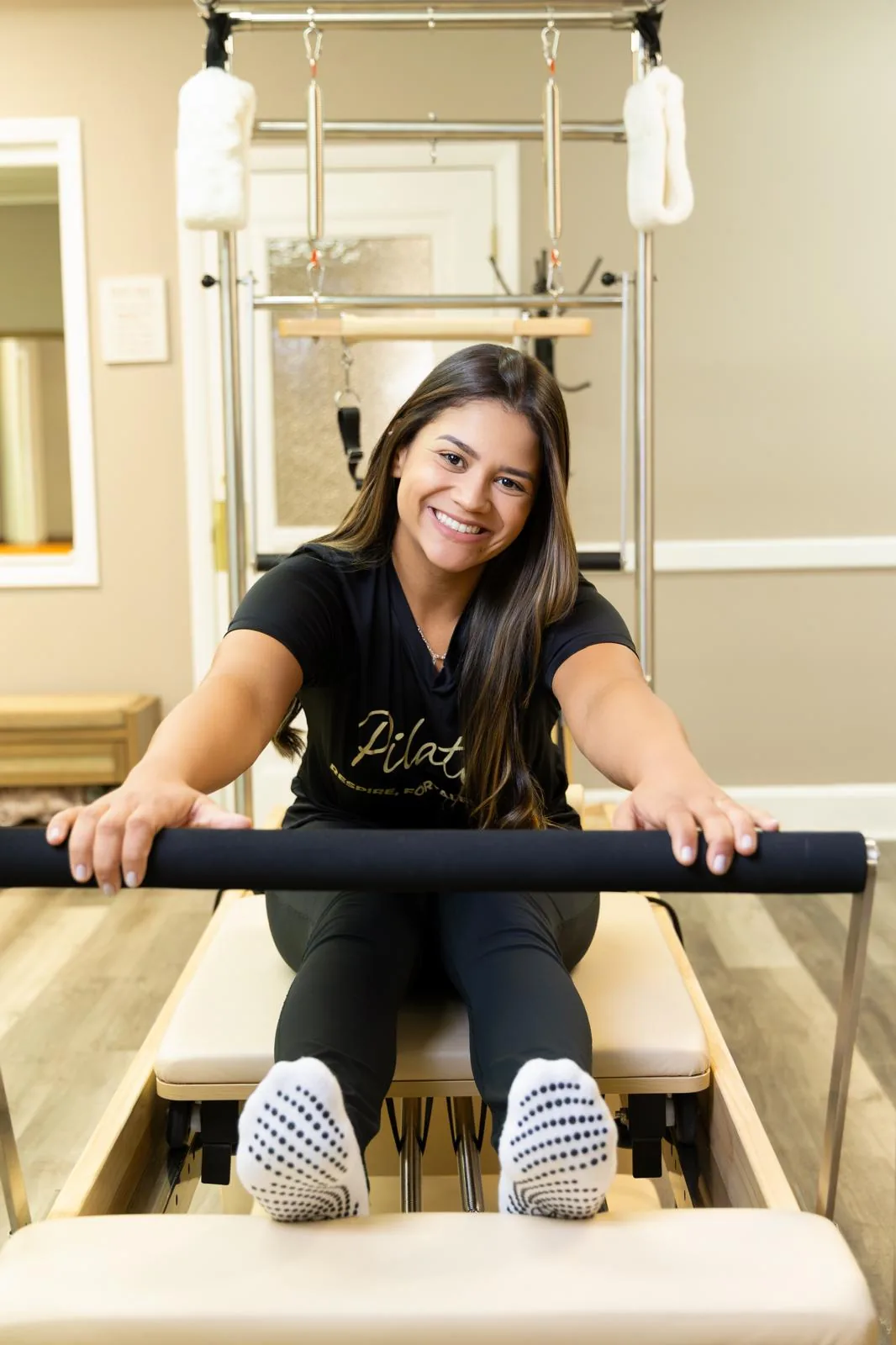 Instructor in fitted workout clothes seated on the Reformer, holding the foot bar