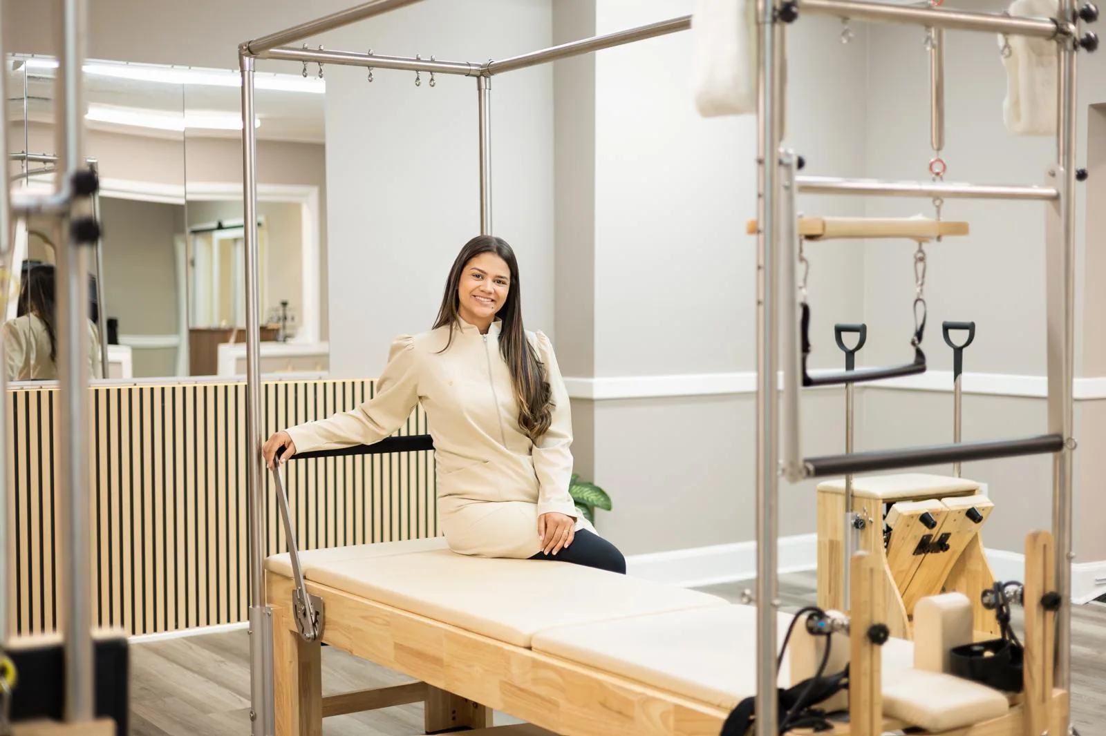 Bruna Felix Costa seated on a Cadillac trapeze table in the main Pilates room